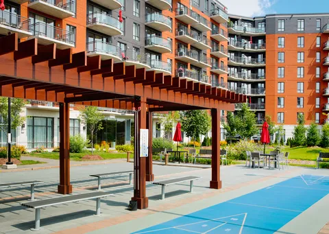 Residence balconies overlooking a courtyard with picnic tables, a pergola and shuffleboard court