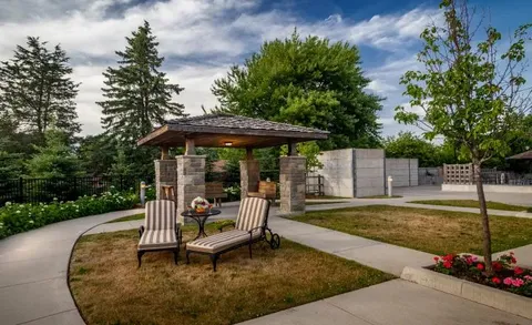 Gazebo and patio chairs beside landscaped paths and trees.