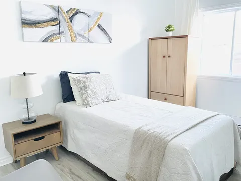 Bedroom with a single bed, wooden wardrobe, bedside lamp and abstract wall art