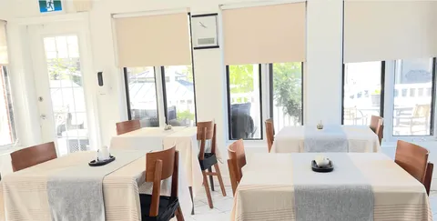 Dining area with white-covered tables, wooden chairs and large windows