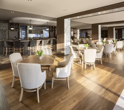 Tables and pale upholstered chairs beside a bar counter and stools