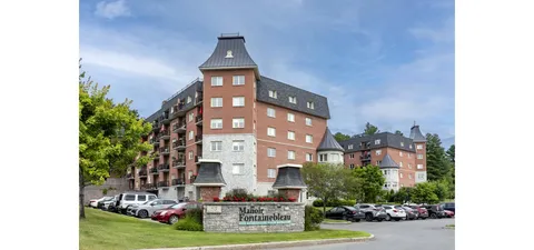 Brick residence with towers, balconies, a stone name sign and parked cars