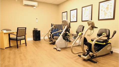 Fitness room with exercise equipment, a table and framed pictures.