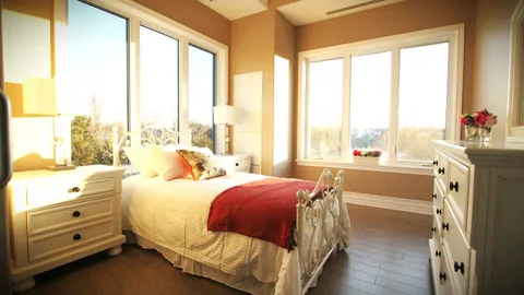 Bedroom with a bed, bedside table and large corner windows.