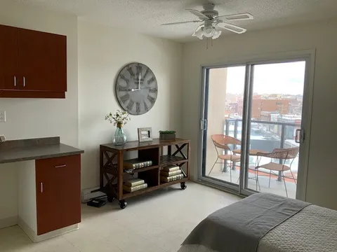 Room with a kitchenette, bed edge, console table and glass doors to a balcony