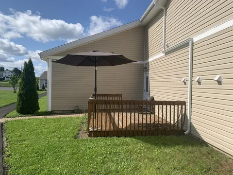 Side of the residence with a wooden patio, umbrella and lawn.