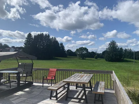 Wooden deck with a picnic table, chairs and a canopy overlooking the lawn.