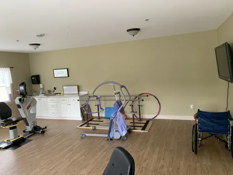 Exercise room with a stationary cycle, parallel bars, a patient lift and a wheelchair.
