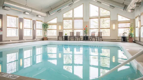 Indoor pool beneath a high ceiling with large windows and poolside chairs