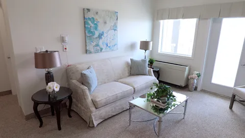 Room with a sofa, glass coffee table, lamps and a window