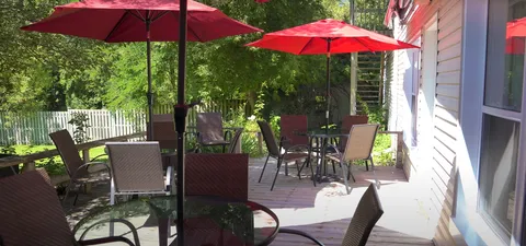 Wooden patio with glass-topped tables, woven chairs and red umbrellas