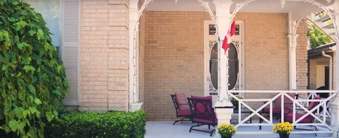 Covered porch with white railings, a bench, flowers and a decorative glass door