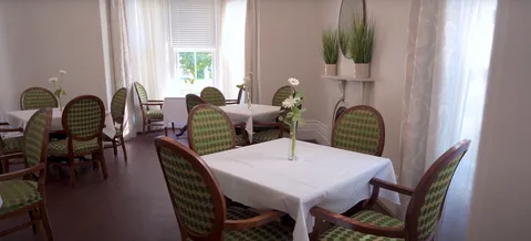 Dining room with white-covered tables, green chairs, curtains and flower vases