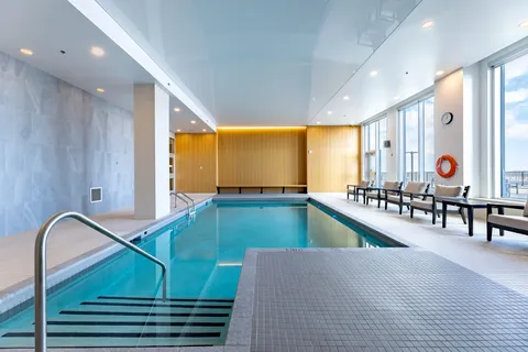 Indoor pool with entry steps and chairs beside large windows