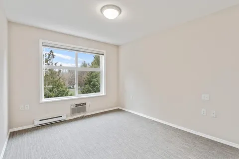 Empty carpeted room with a large window and white walls