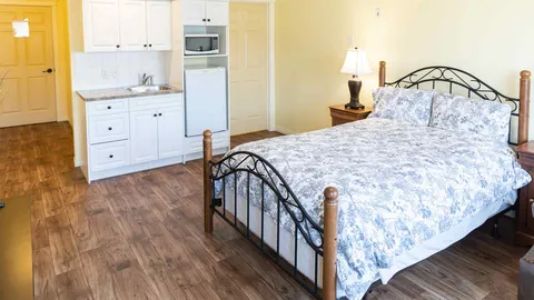 Bedroom with a metal-framed bed beside a white kitchenette with a sink, microwave and small refrigerator