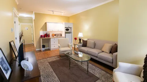 Room with a sofa, armchairs, glass coffee table, television and white kitchenette