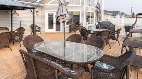 Wooden deck with wicker chairs, round glass tables, closed umbrellas and a covered seating area