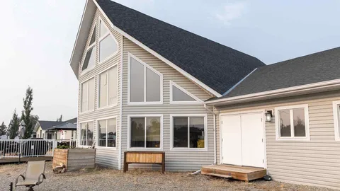 Grey-sided building with a steep gable roof, large windows, wooden bench and adjacent deck