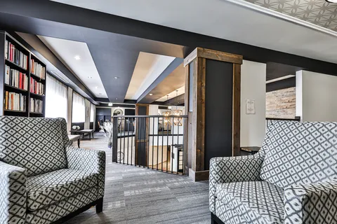 Seating area beside bookshelves, a railing and tall windows