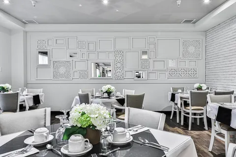 Dining room with set tables, pale chairs and mirrors on the wall