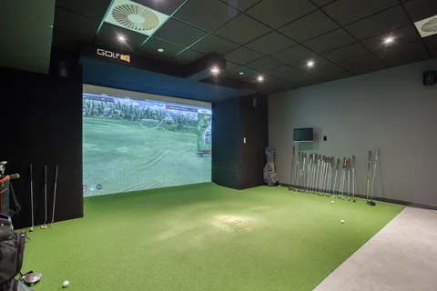 Indoor golf simulator with a putting surface and golf clubs.