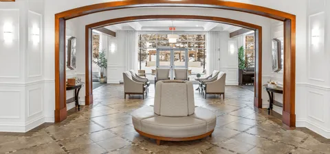 Lobby with a round upholstered seat, white armchairs and wooden arches