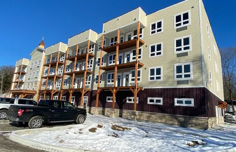 Residence building with wooden balconies beside parked vehicles and snow