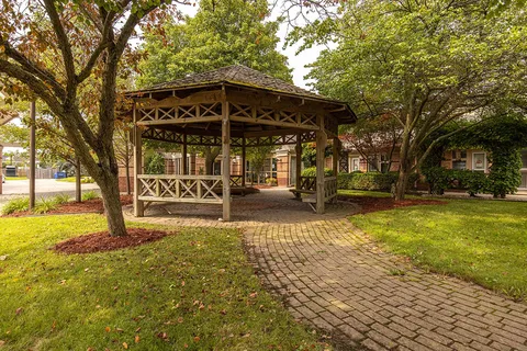 Garden gazebo beside a paved path and mature trees.