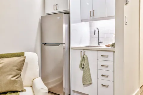 Kitchenette with white cabinets, sink and refrigerator.