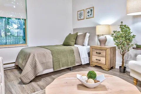 Studio bedroom with a bed, seating, lamps and a window.