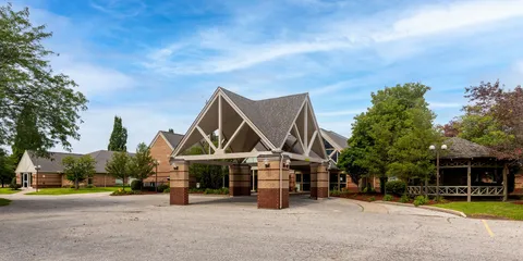 Residence building and covered entrance beside a driveway and mature trees.