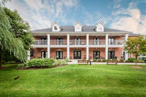 Brick residence building with a columned balcony behind a landscaped lawn
