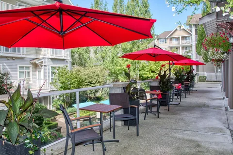 Patio walkway with chairs, tables and red umbrellas.
