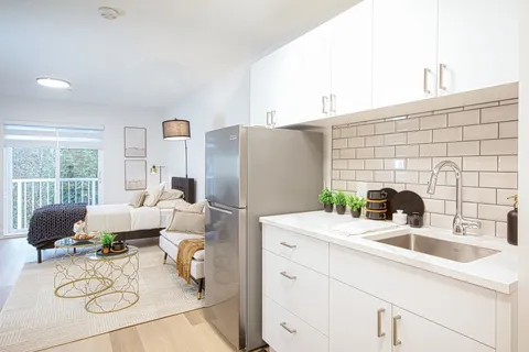 Suite kitchen with white cabinets beside a living area.