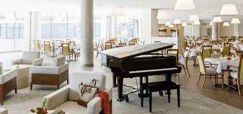 Grand piano and cream seating beside dining tables and tall windows