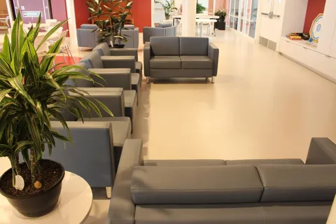 Sitting area with gray sofas, armchairs, potted plants and cream flooring