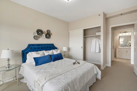 Bedroom with a blue upholstered headboard, bedside lamps, open closet and bathroom doorway