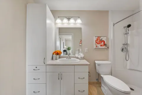 Bathroom with white cabinets, a sink, wall mirror, toilet and shower