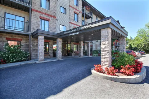 Covered glass entrance beside flower beds and the front driveway.