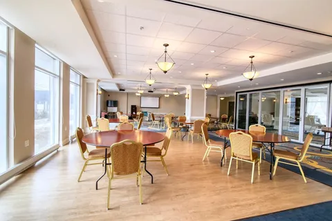 Activity room with round tables, upholstered chairs and a projection screen.
