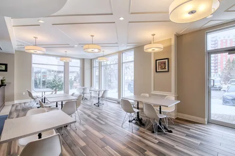 Bistro seating area with white tables and chairs beside large windows.