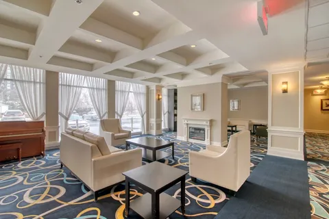 Lounge with armchairs, coffee tables and a fireplace beside large windows.