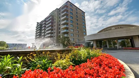 Residence tower and covered entrance behind a fountain and flowerbeds.