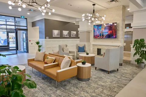 Lobby seating with a fireplace, plants and large windows.