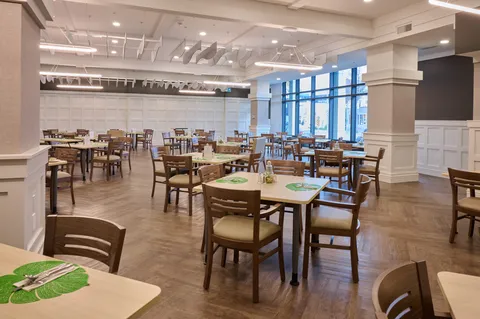 Dining room with tables, wooden chairs and tall windows.