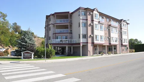 Residence building viewed across the street beside trees and an entrance sign.