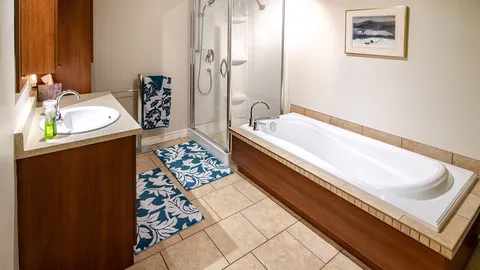Bathroom with bathtub, glass shower, vanity and framed landscape