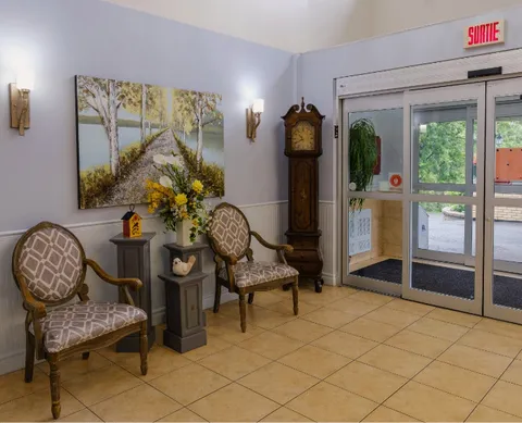 Entrance lobby with two chairs, a grandfather clock, landscape art and glass doors.