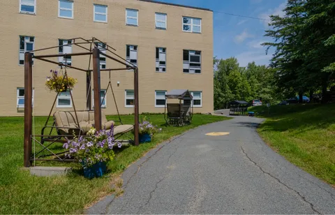 Garden path beside the building with covered swings, hanging flowers and lawn.